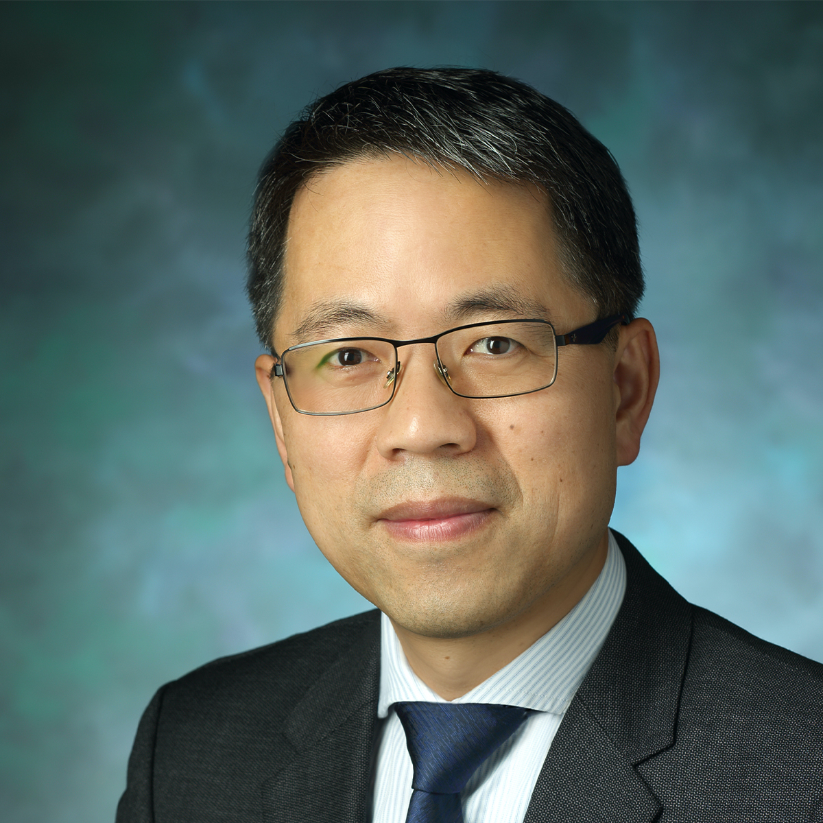 Headshot of Hai-Quan Mao. He has salt and pepper hair and brown eyes. He is wearing black square frame glasses and a gray suit jacket with a blue shirt and dark blue tie.