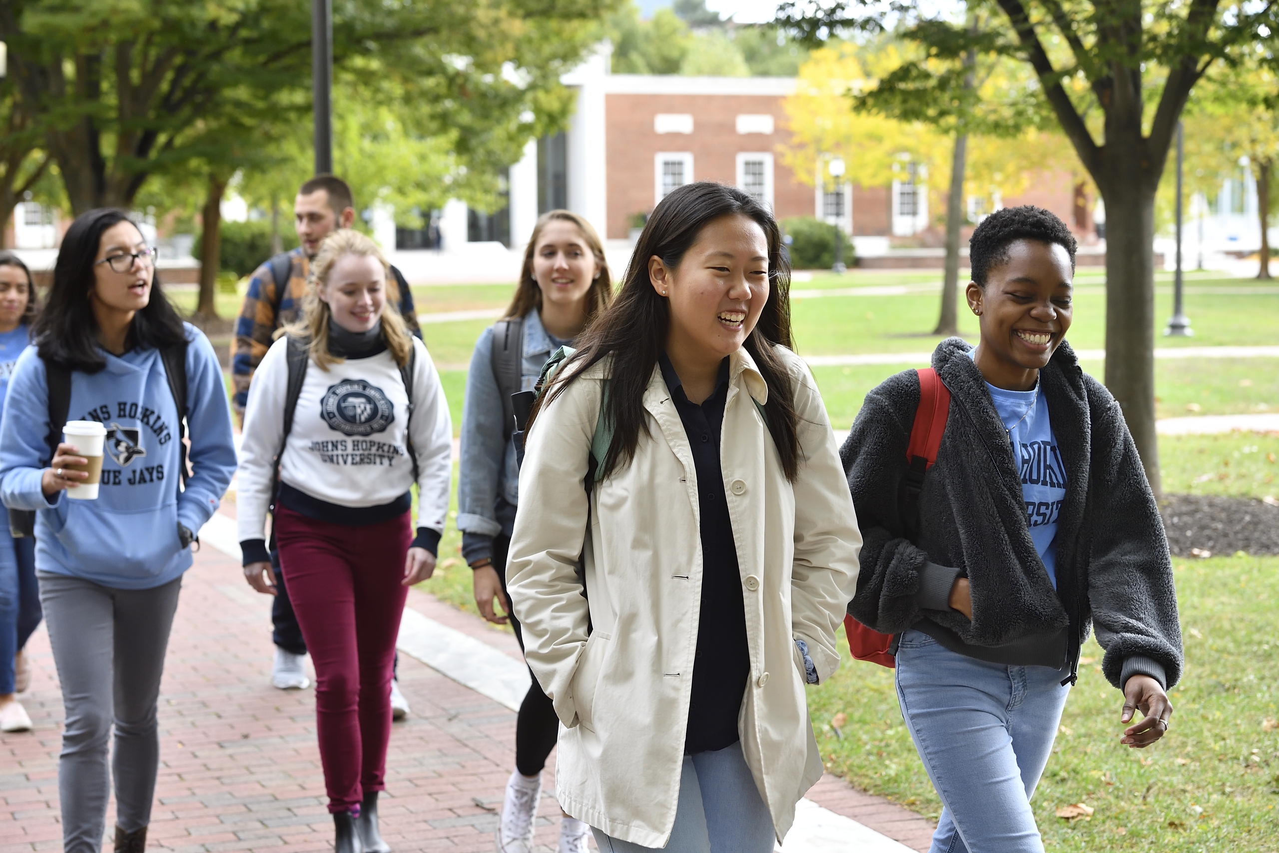 Six students wearing fall clothes walking down brick side walk on a college quad.